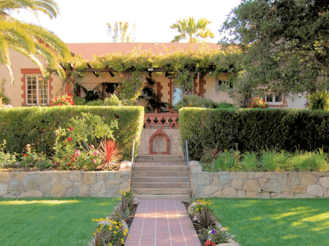 Alexander Gardens, built in 1906, with its neautioful lawn, stone wall, and hedges in the fireground, and the one-story Mediterranean-style home in the background